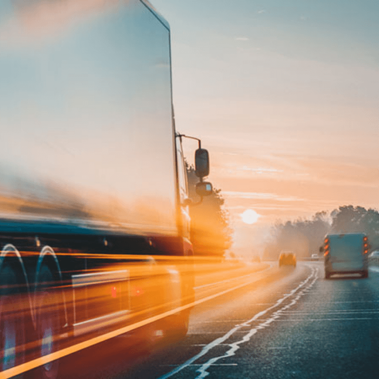 A semi truck going fast down the highway in the evening.
